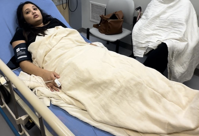 A woman with light brown skin lying in a blue hospital bed.